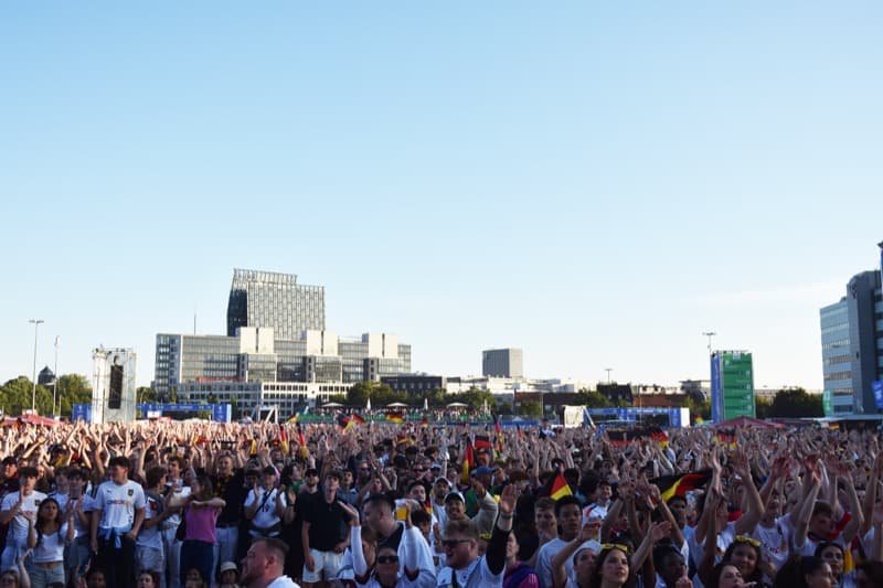 Crowd of fans with German flags and jerseys at the Berlin fan mile by the Brandenburg Gate.