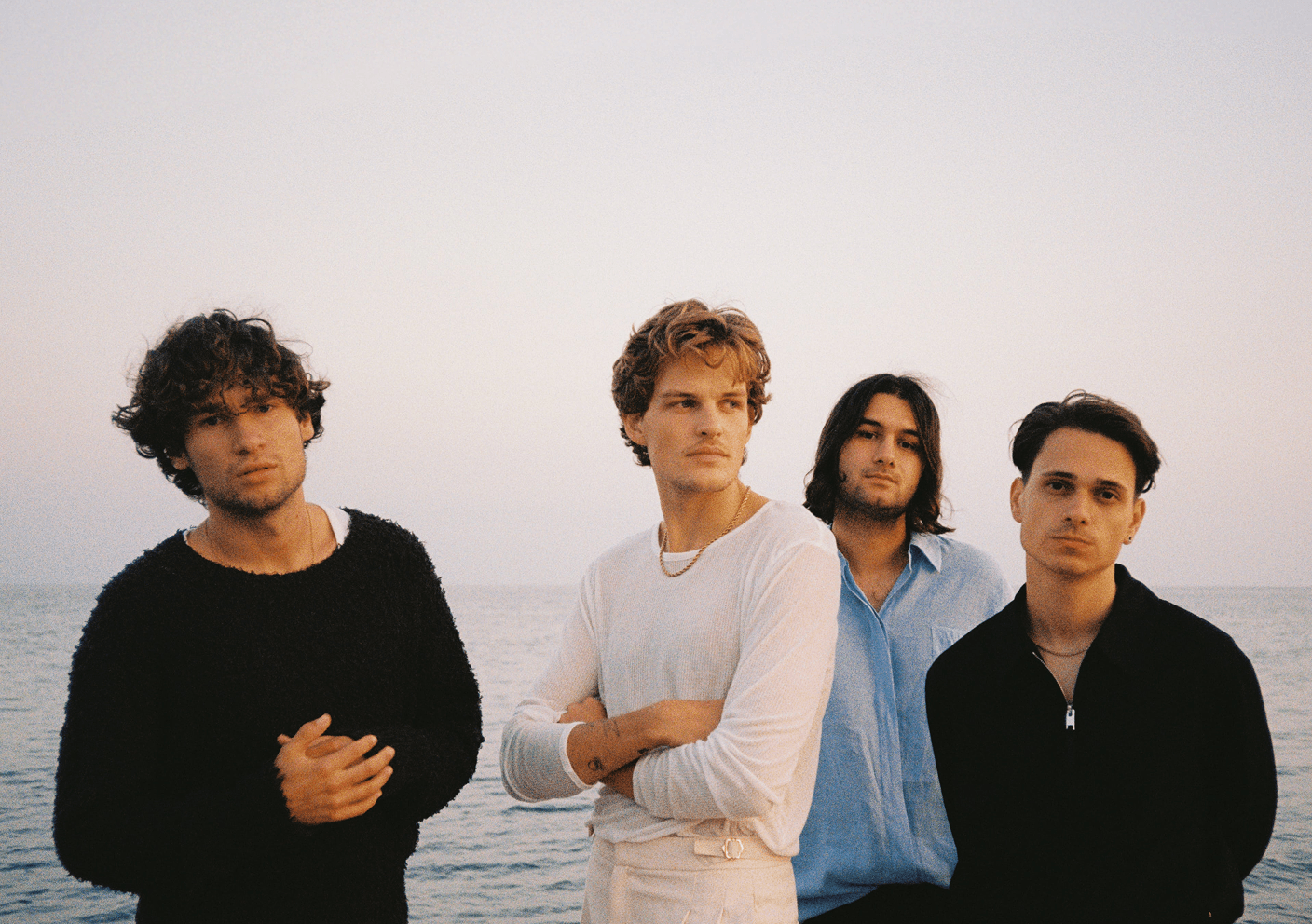 The four members of Jeremias standing by the sea at sunset, looking seriously at the camera.