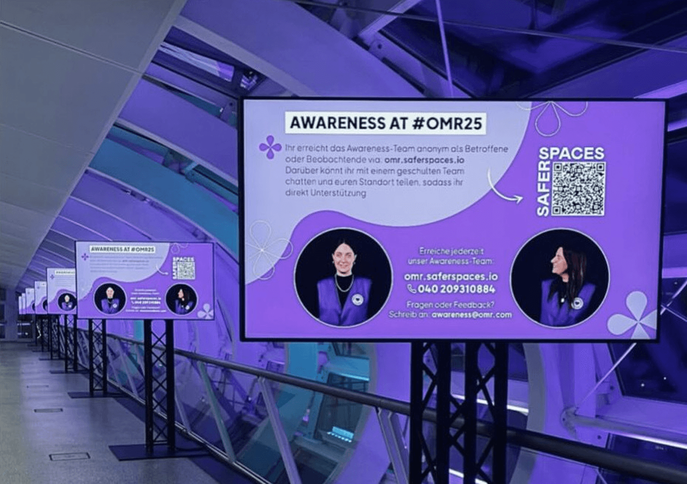 Digital info boards with a purple background at #OMR25 explaining awareness and contact options.