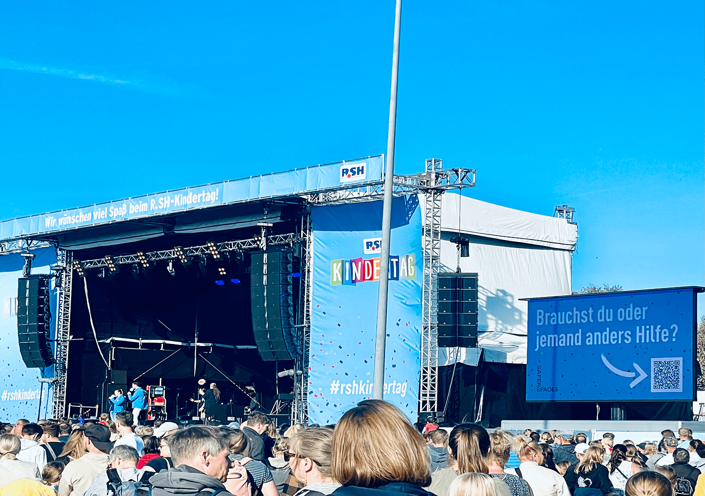 Stage at the R.SH Kindertag with audience and a banner reading 'We wish you a lot of fun at the R.SH-Kindertag'.