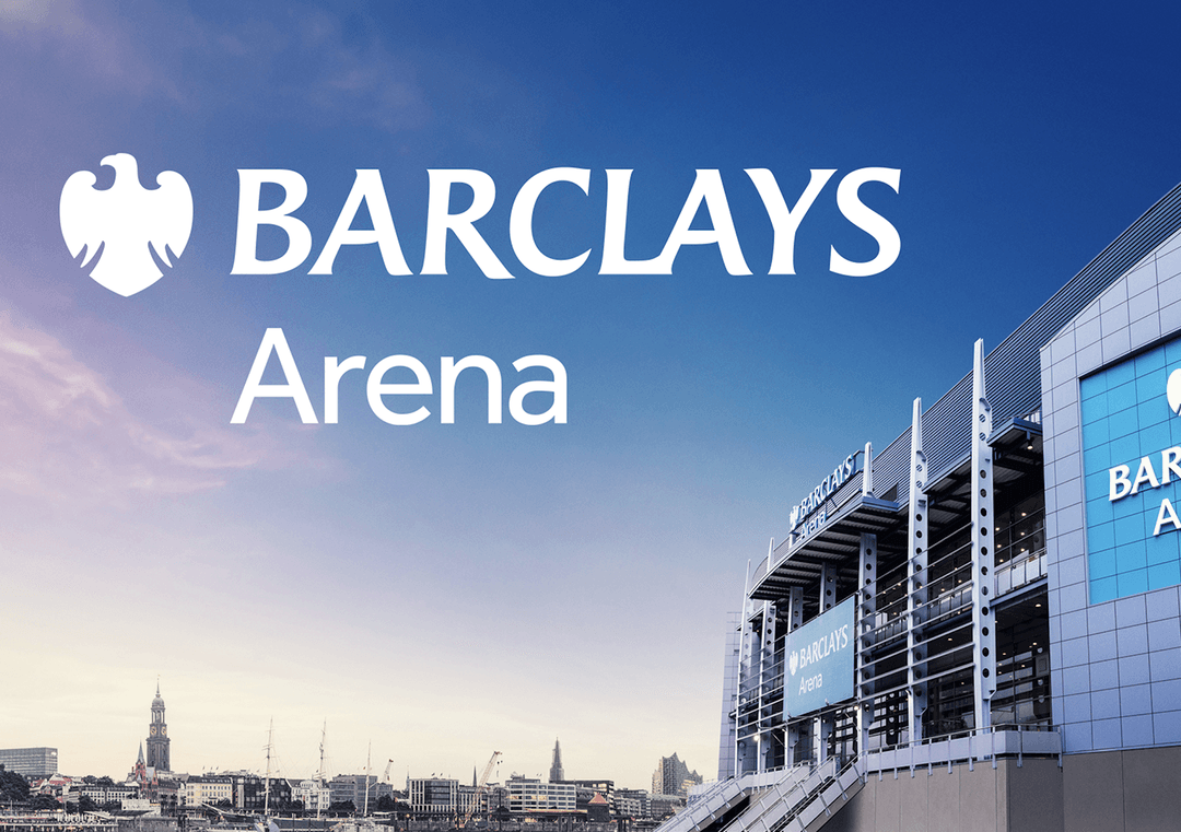 Barclays Arena with large logo and text, modern building in front of city silhouette against blue sky.