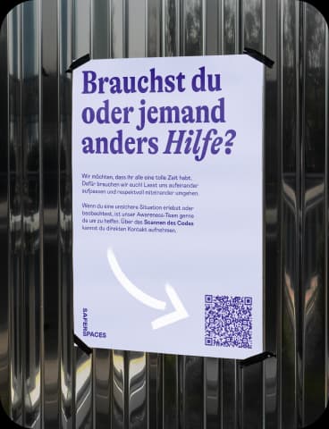 Ein Plakat hängt an einer Wand. Auf diesem steht 'Brauchst du oder jemand anders Hilfe?'. In der rechten unteren Ecke ist ein QR Code.