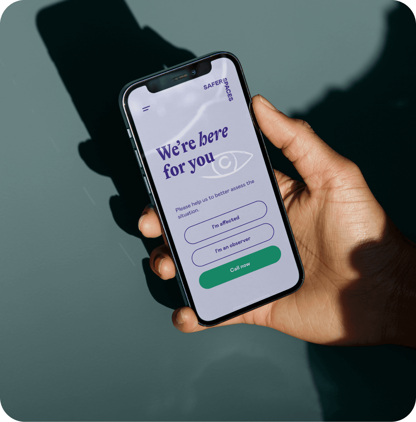 A hand is holding a smartphone. The saferspaces WebApp is open on the display. At the top it reads 'We are here for you'. Below that are three options: 1. I am affected, 2. I am an observer, 3. Call directly.